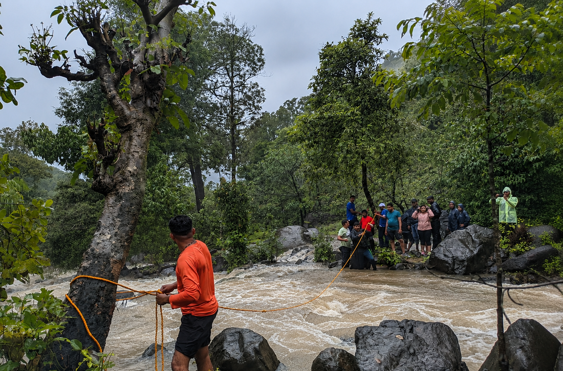 Guide and trekking group crossing a monsoon-swollen river using a safety rope